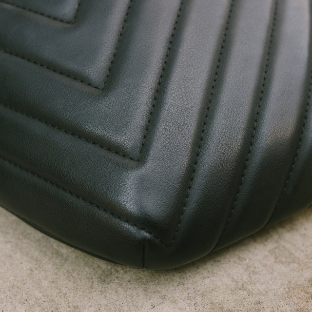 Close shot of the bottom of the Honeypie Bum Bag focused on the stitching for the quilted pattern and the leathery texture of the black faux leather