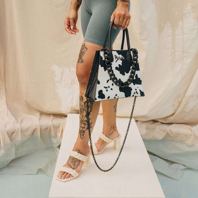 Cowprint handbag with a chunky black accent chain and slender long chain for over the shoulder use shown on a woman with tattoos